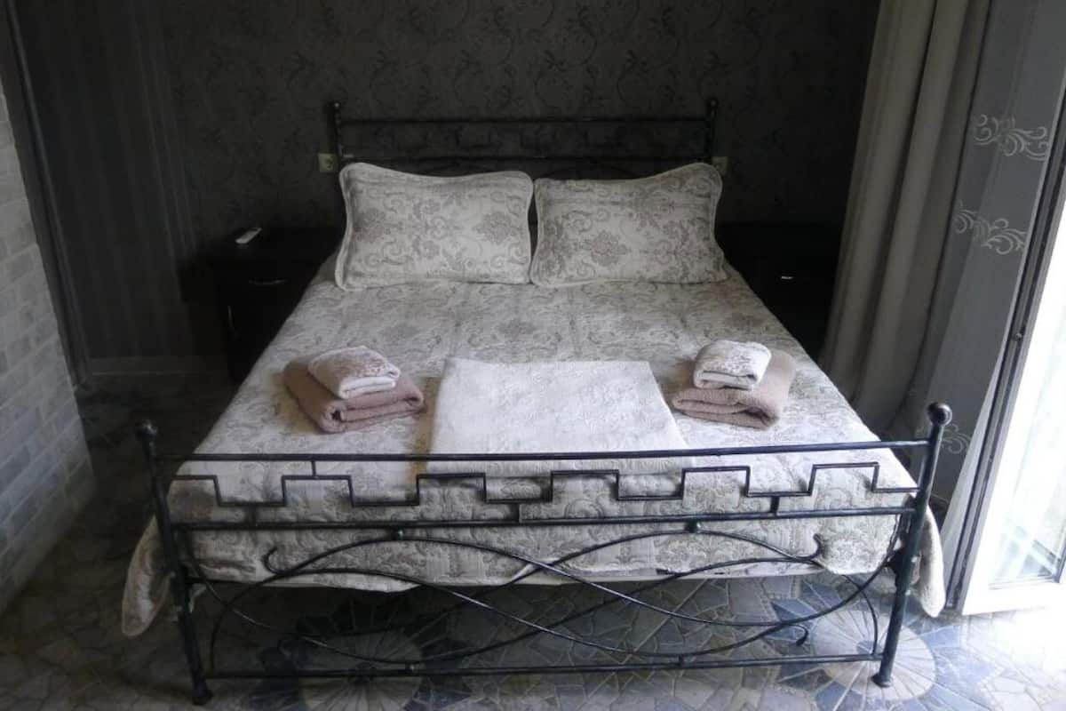A single bed with a patterned bedspread and pillows, a bedside table, and a window with curtains.