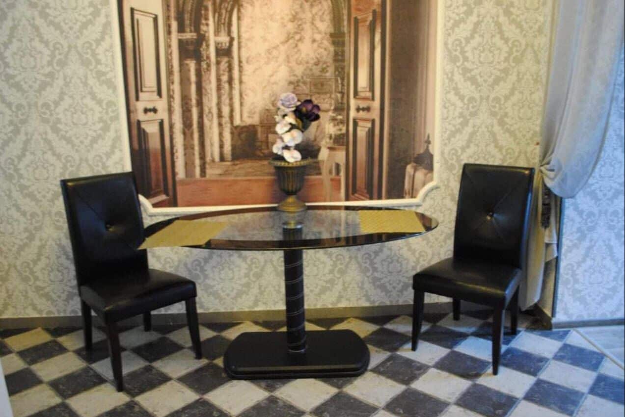 A room with a round table, two chairs, a vase with flowers, and patterned wallpaper.