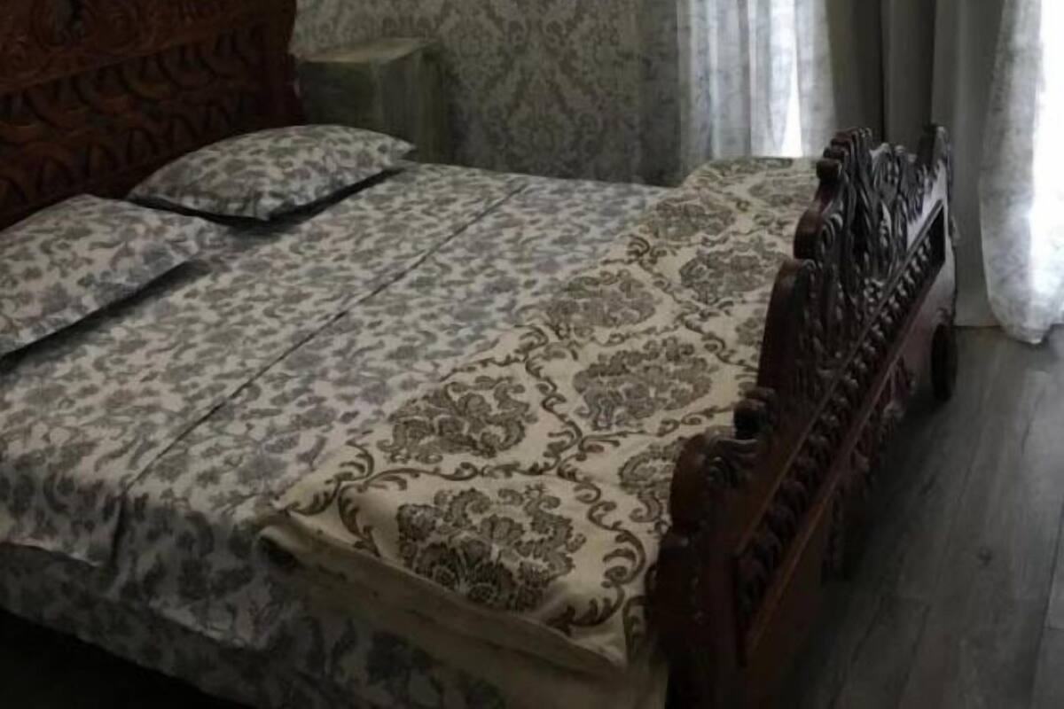 A bedroom with a patterned wallpaper, a wooden headboard, a bed with a patterned bedspread, a bedside table, and a wall-mounted light fixture.