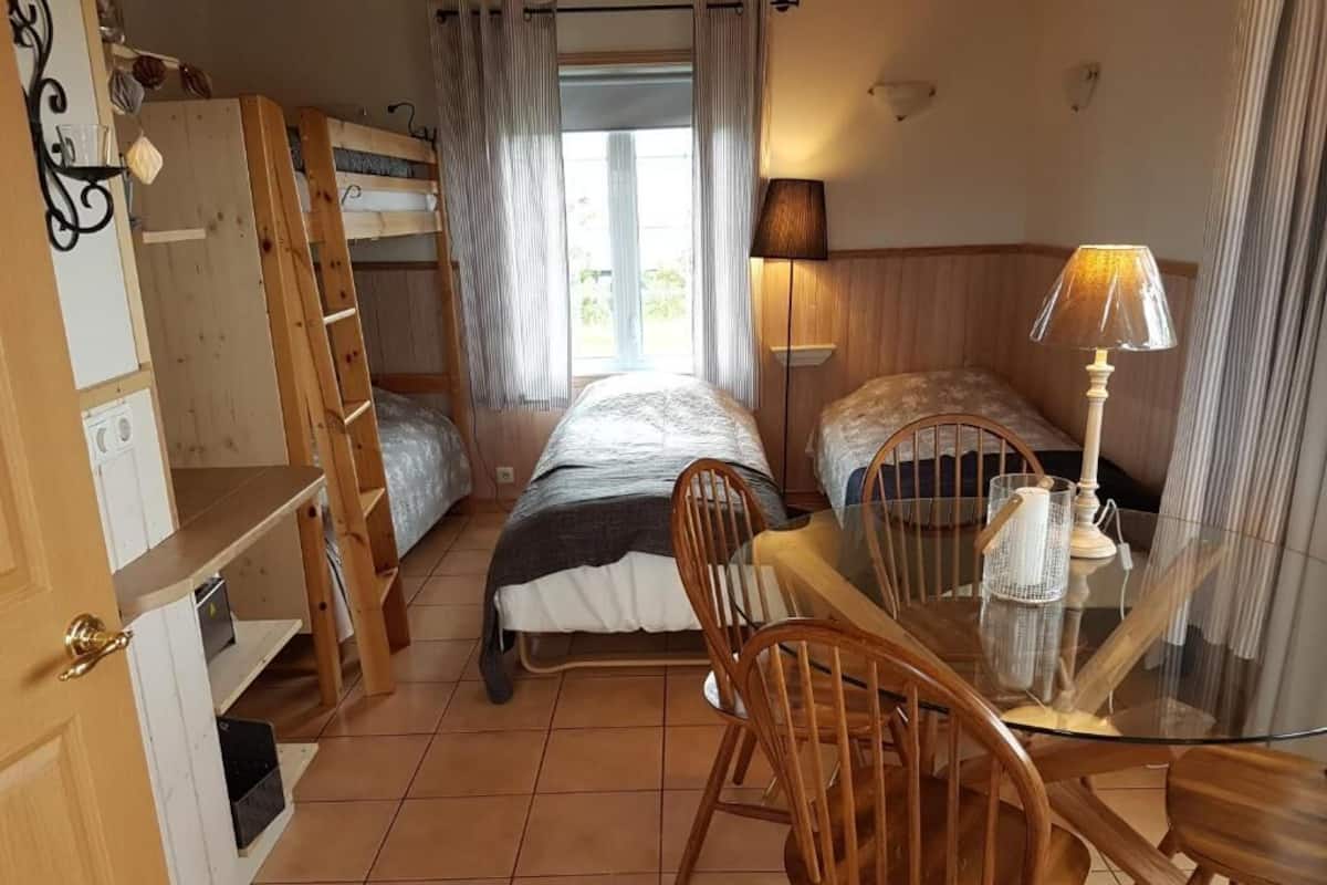 A compact room with bunk beds, a small dining table with chairs, a lamp, and a window with curtains.