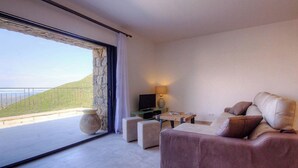Una sala de estar moderna con un sofá, una mesita de centro y un televisor. Se ve una ventana grande con vistas a un paisaje verde.
