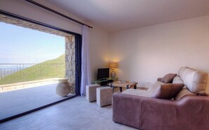 A modern living room with a sofa, a coffee table, and a TV. There is a large window with a view of a green landscape. - Residence Casa Di Roc (Urtaca)