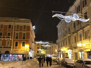 A snow-covered street with buildings and parked cars.