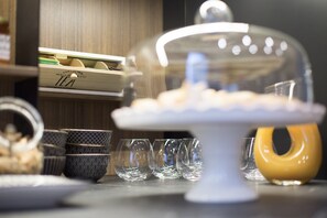 A table with a white cake stand, clear glasses, and a yellow teapot.
