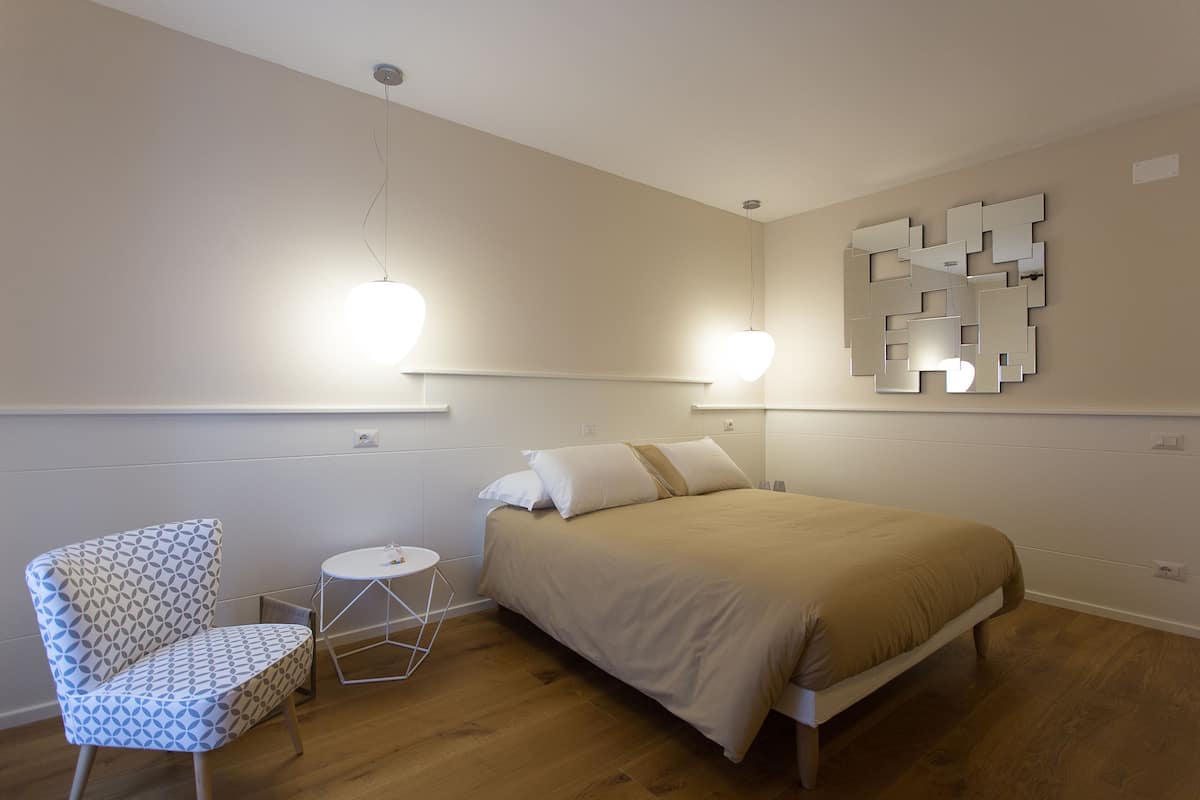 Quarto com cama, uma cadeira e luminária fixada na parede.