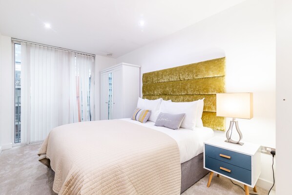 A modern bedroom with a large bed, a bedside table with a lamp, and a wardrobe.