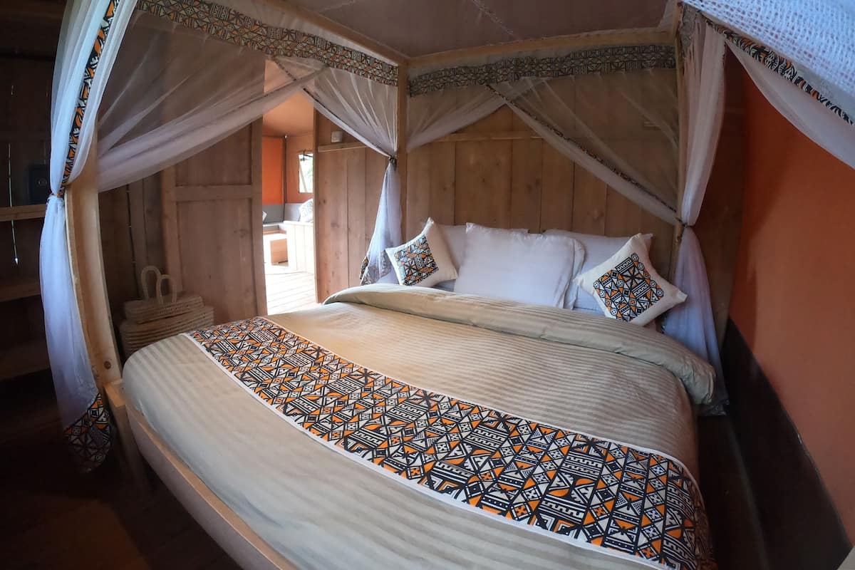 Een bed met een geborduurd beddegoed, een hemelbed en kussens met geometrische patronen.