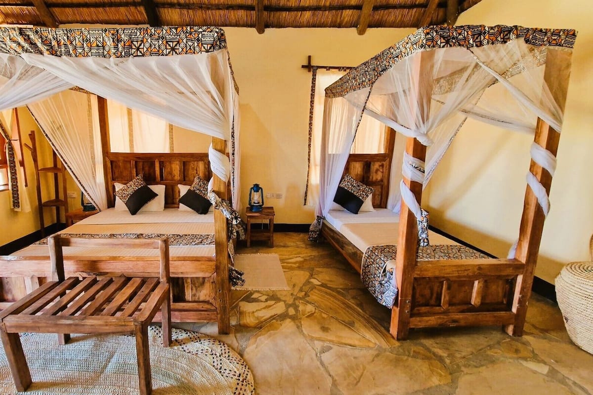 Een traditioneel houten bed met hemelbed, een houten bankje en een geweven mat op de vloer.