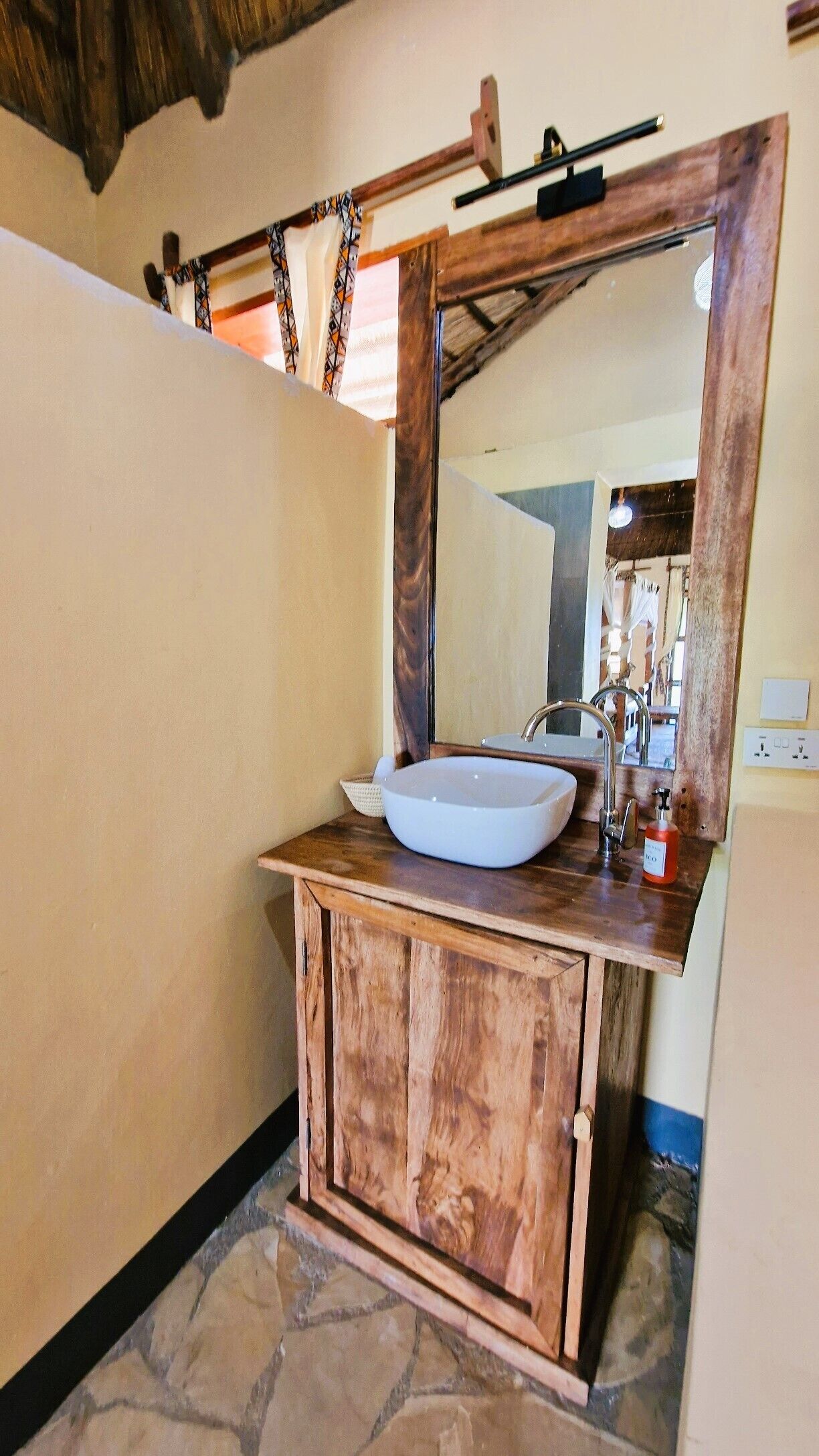 A bathroom with a stone floor, wooden vanity, and a large mirror.