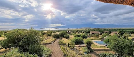 Un resort con piscina, una estructura de techo de paja y vistas al mar y colinas lejanas.