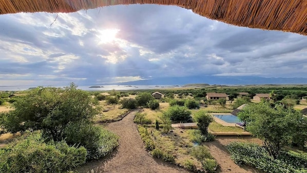 A resort with a pool, a thatched-roof structure, and a view of the sea and distant hills.