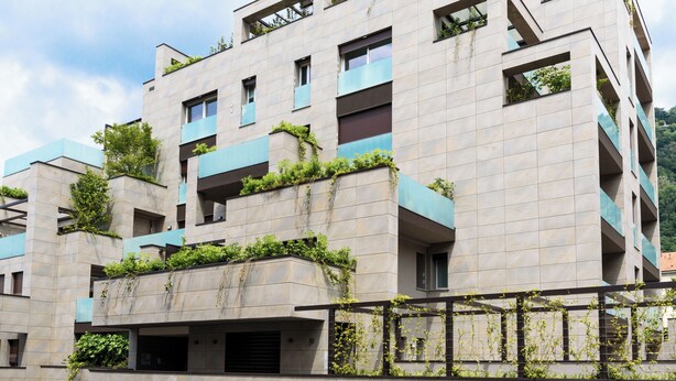 Een modern meerlaags gebouw met balkons, waarvan sommige begroeiing hebben.