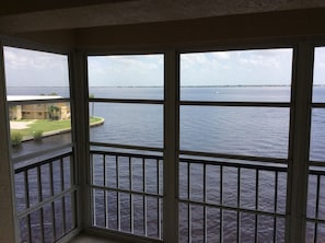 Vista de uma varanda com corrimão, com vista para um corpo de água e uma linha de costa distante.