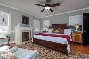 Une chambre à coucher avec un grand lit, une cheminée, un ventilateur de plafond et une table de chevet avec une lampe.