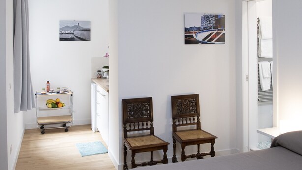 A bedroom with a bed, two wooden chairs, a desk with a chair, a hanging light fixture, and two wall-mounted pictures. - Vesuvio Blu Apartment in the center of Naples (Napoli)