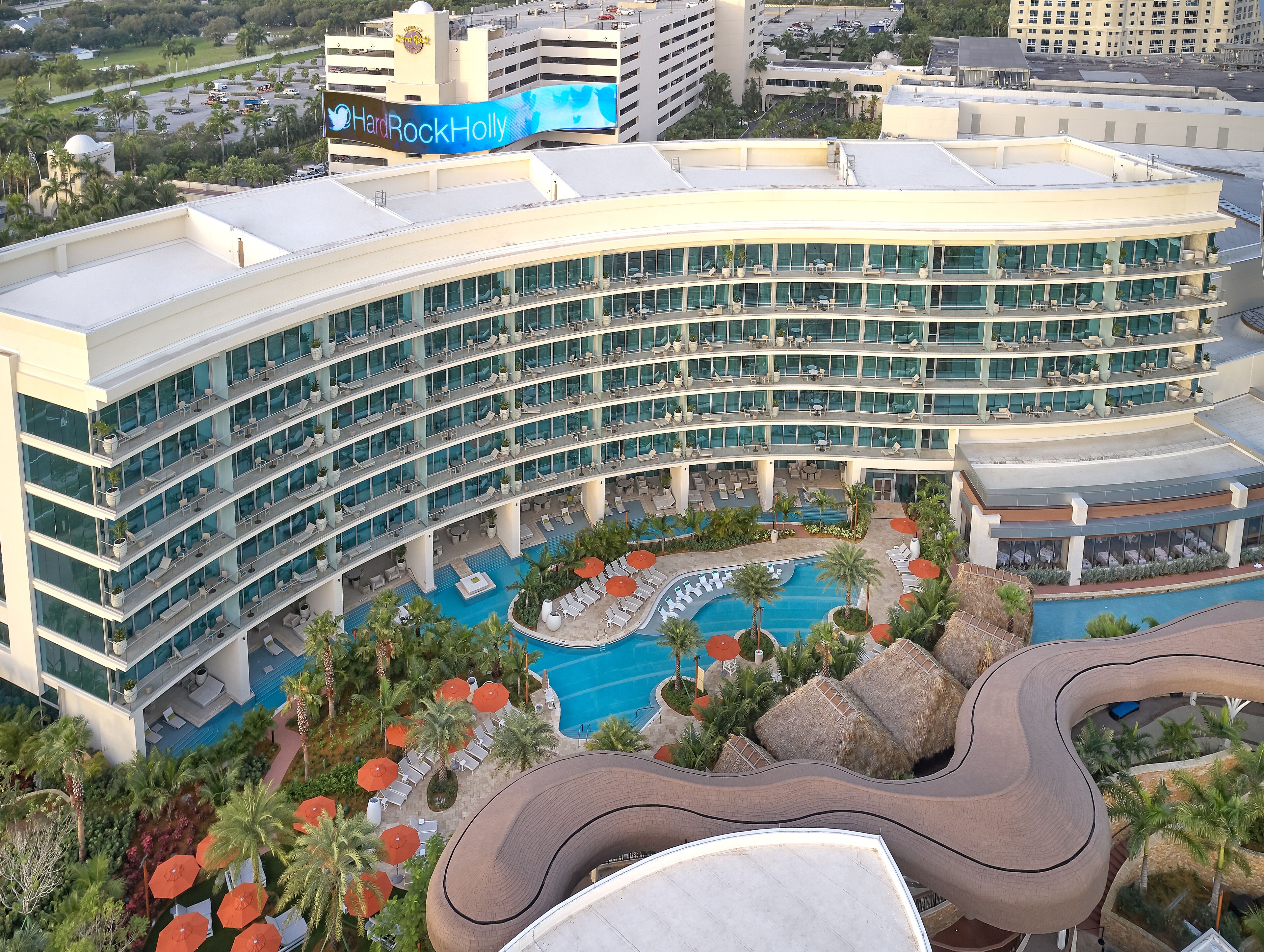 A multi-story hotel with a pool area, outdoor seating, and a curved roof design.