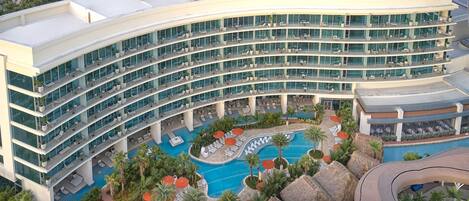 A multi-story hotel with a pool area, outdoor seating, and a curved roof design.