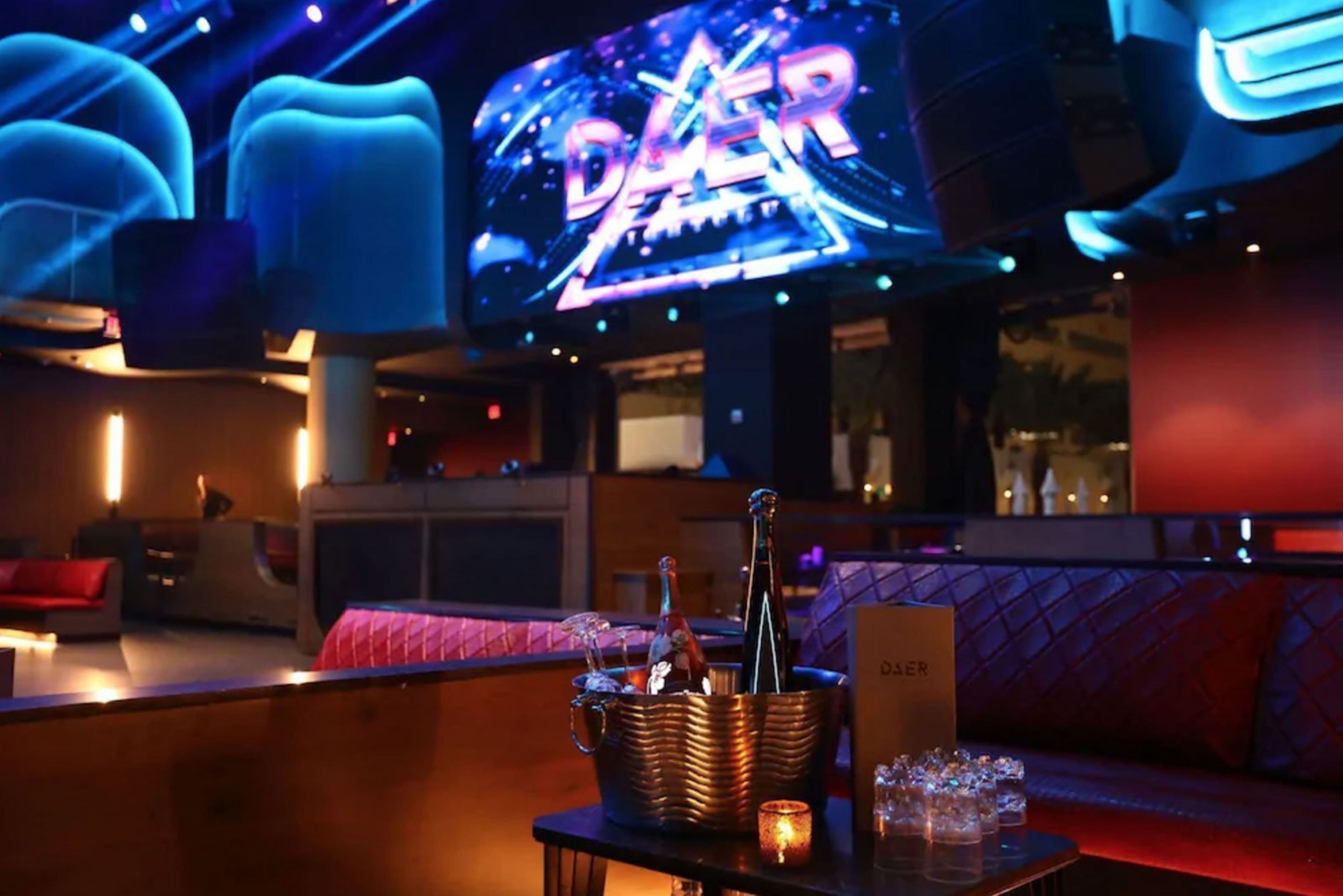 Una zona de bar con un letrero de neón, una botella de champán y copas sobre una mesa.