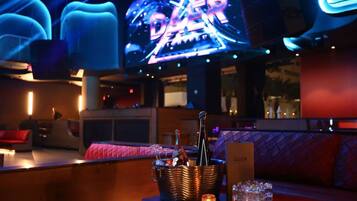 Una zona de bar con un letrero de neón, una botella de champán y copas sobre una mesa.