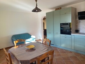 Un comedor con una mesa, sillas, un sofá azul y una cocina con armarios azul claro y un horno negro.