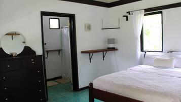 Un dormitorio con una cama de madera, un tocador, un espejo, una ventana con cortinas y un pequeño estante.