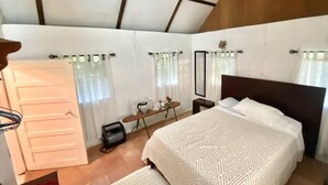A bedroom with a large bed, a wooden headboard, a bedside table with a mirror, and a window with curtains.