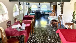 A dining area with tables covered in red tablecloths, wooden chairs, and a laptop on one table.