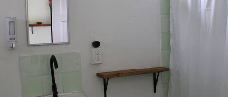 A bathroom with a white sink, a mirror, a window, a shower curtain, and a wooden shelf.