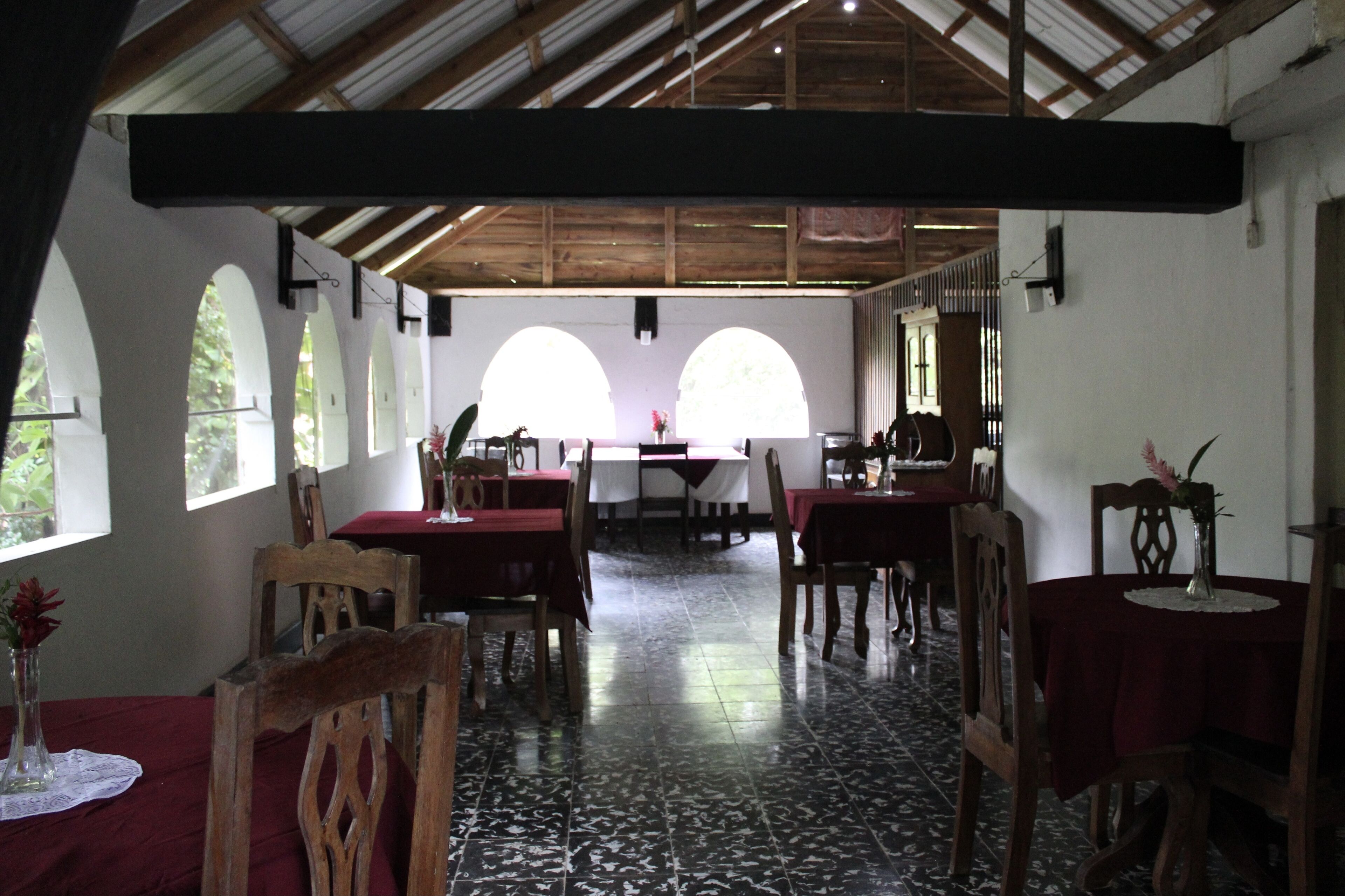 Un comedor con mesas y sillas de madera, amplias ventanas de arco y un techo alto con vigas de madera.