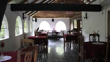 Un comedor con mesas y sillas de madera, amplias ventanas de arco y un techo alto con vigas de madera.