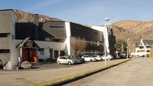 A hotel with a modern design, a red entrance, and a parking lot with several cars. - Family apartment in Saint-Lary for 6 people, near the gondola and thermal baths. (Saint-Lary-Soulan)