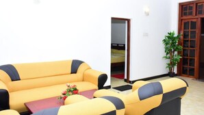 A yellow sofa with black accents in a room with white walls and a wooden door. - Rio Home stay (Haputhale)