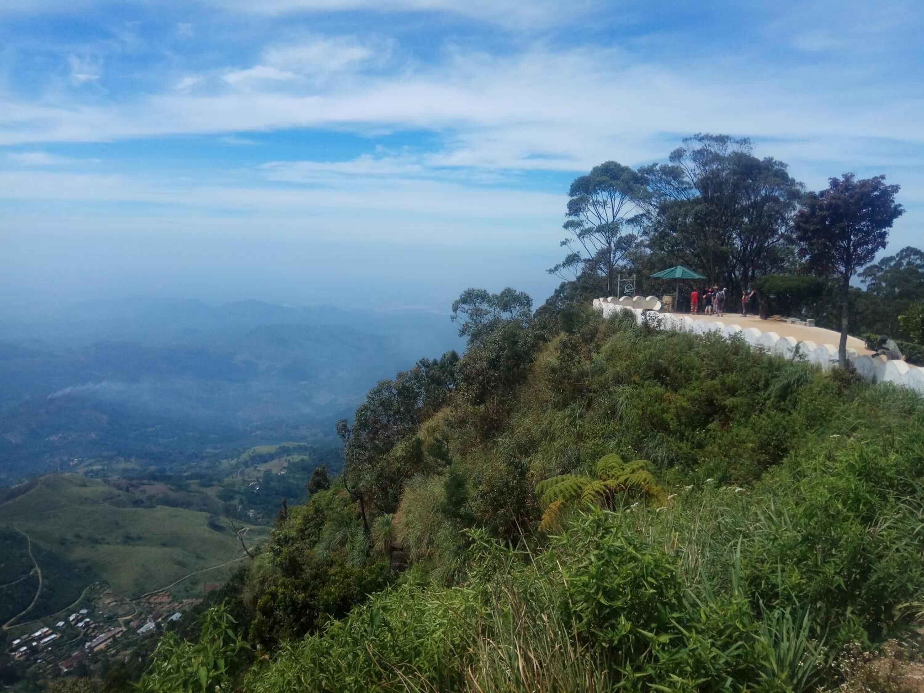 Un punto panorámico con un sendero blanco, abundante vegetación y un valle distante.