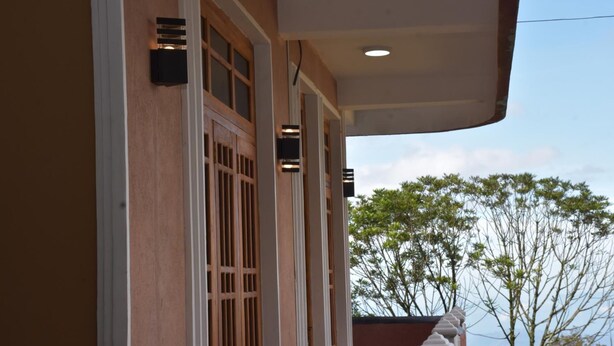 A building with a wooden facade, a balcony with a railing, and a clear sky in the background. - Rio Home stay (Haputhale)