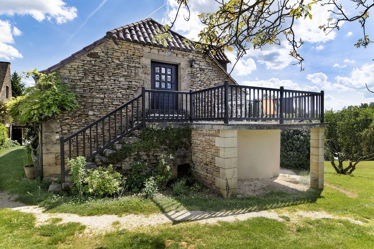 A stone house with a black metal balcony and a small staircase leading to a door.