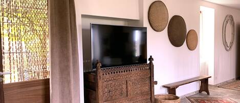 A living room with a television on a wooden cabinet, a bench, and a woven basket.