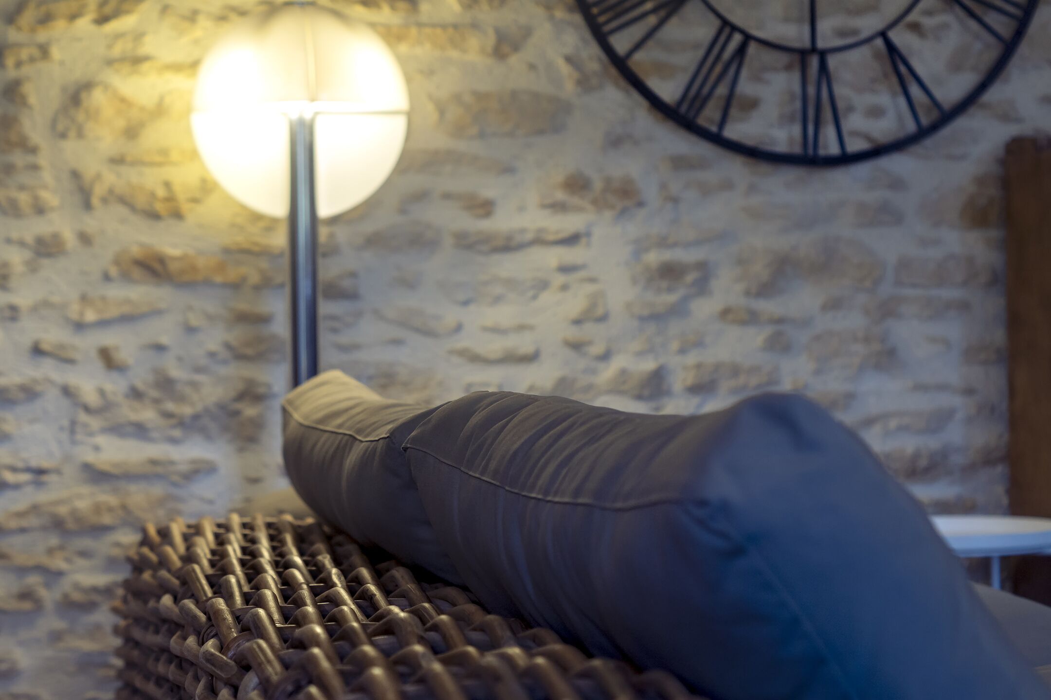 Une pièce avec un mur en pierre, une horloge murale ronde et un lampadaire.