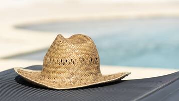 Un sombrero de paja sobre una silla de descanso negra junto a una piscina.
