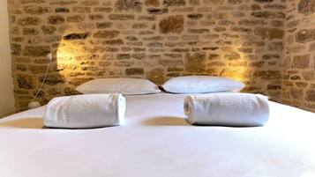 Una habitación con pared de piedra, una cama con sábanas blancas y dos toallas enrolladas sobre la cama.