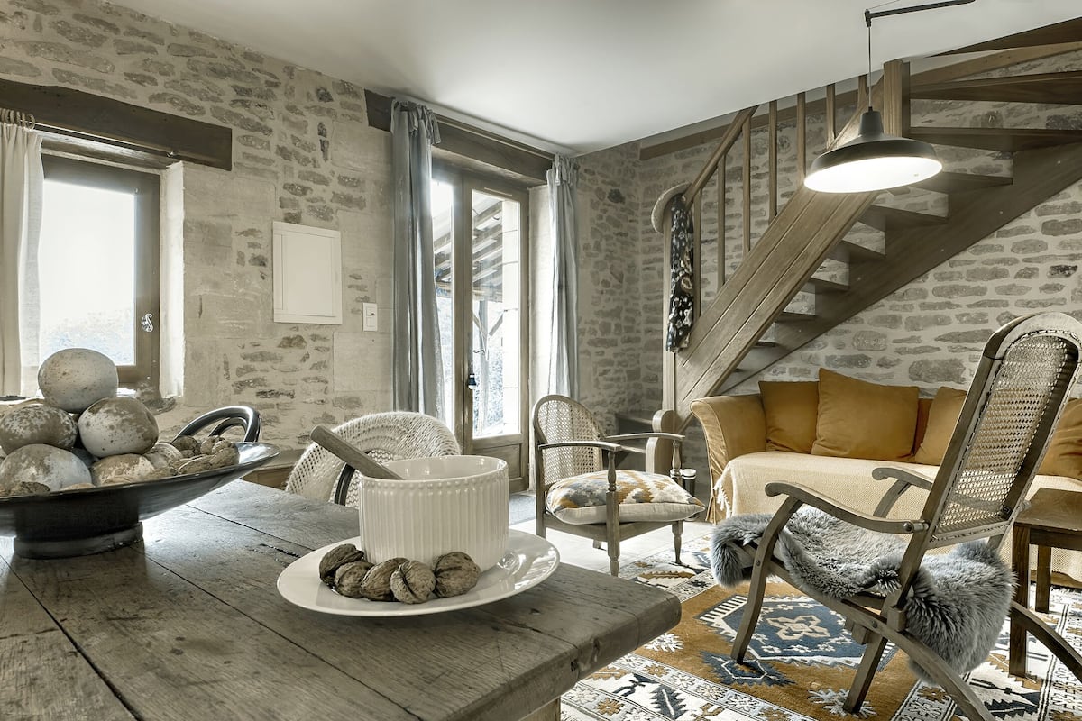 A rustic interior with a stone wall, wooden staircase, and a dining area with a table set for a meal.