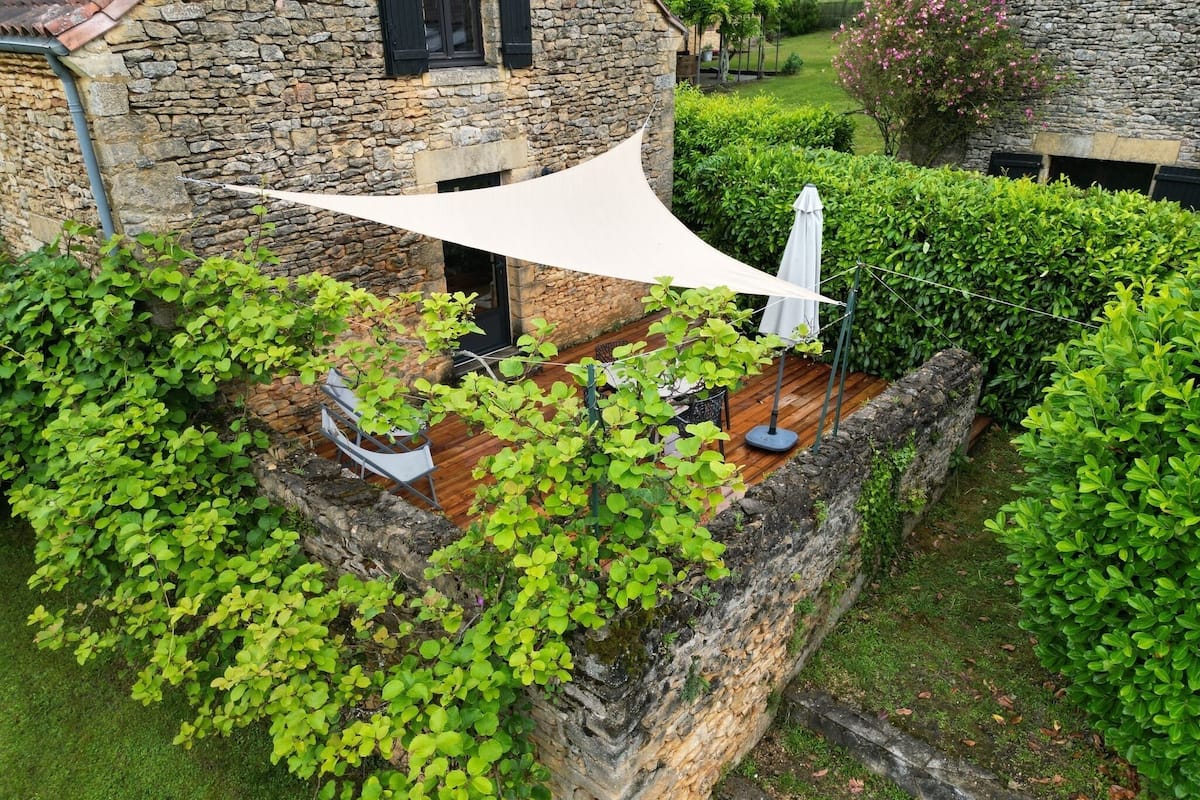A stone building with a wooden deck, surrounded by lush greenery and a white canopy providing shade.