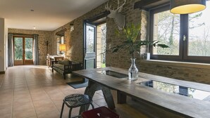 A spacious room with a large wooden table, a red stool, and a potted plant.