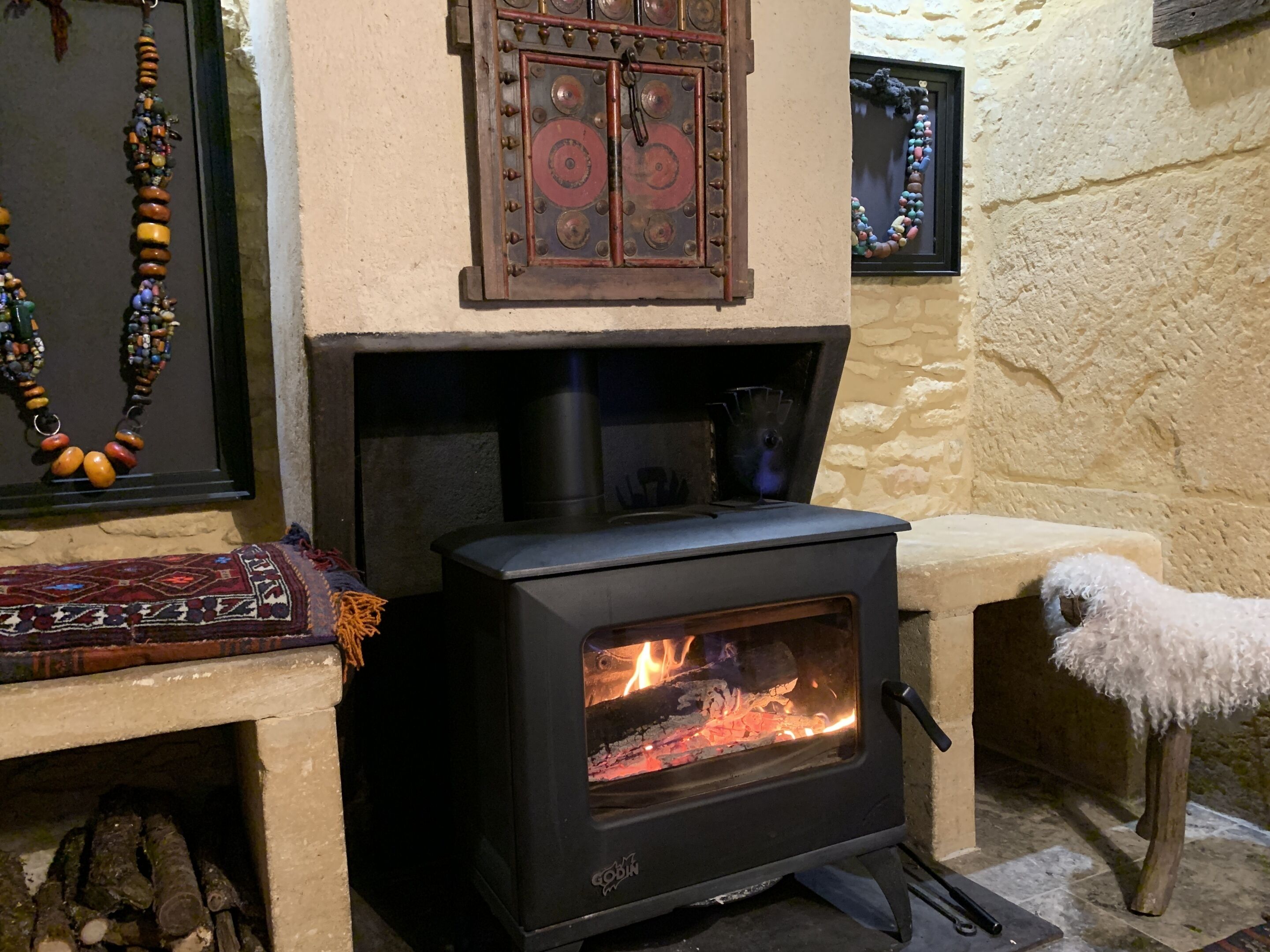 A wood-burning stove with a glass door, a rustic wooden door above it, and a white fluffy dog nearby.