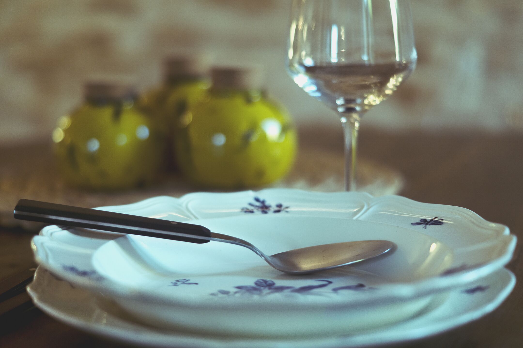A dining table with a plate, a spoon, and a glass of white wine.