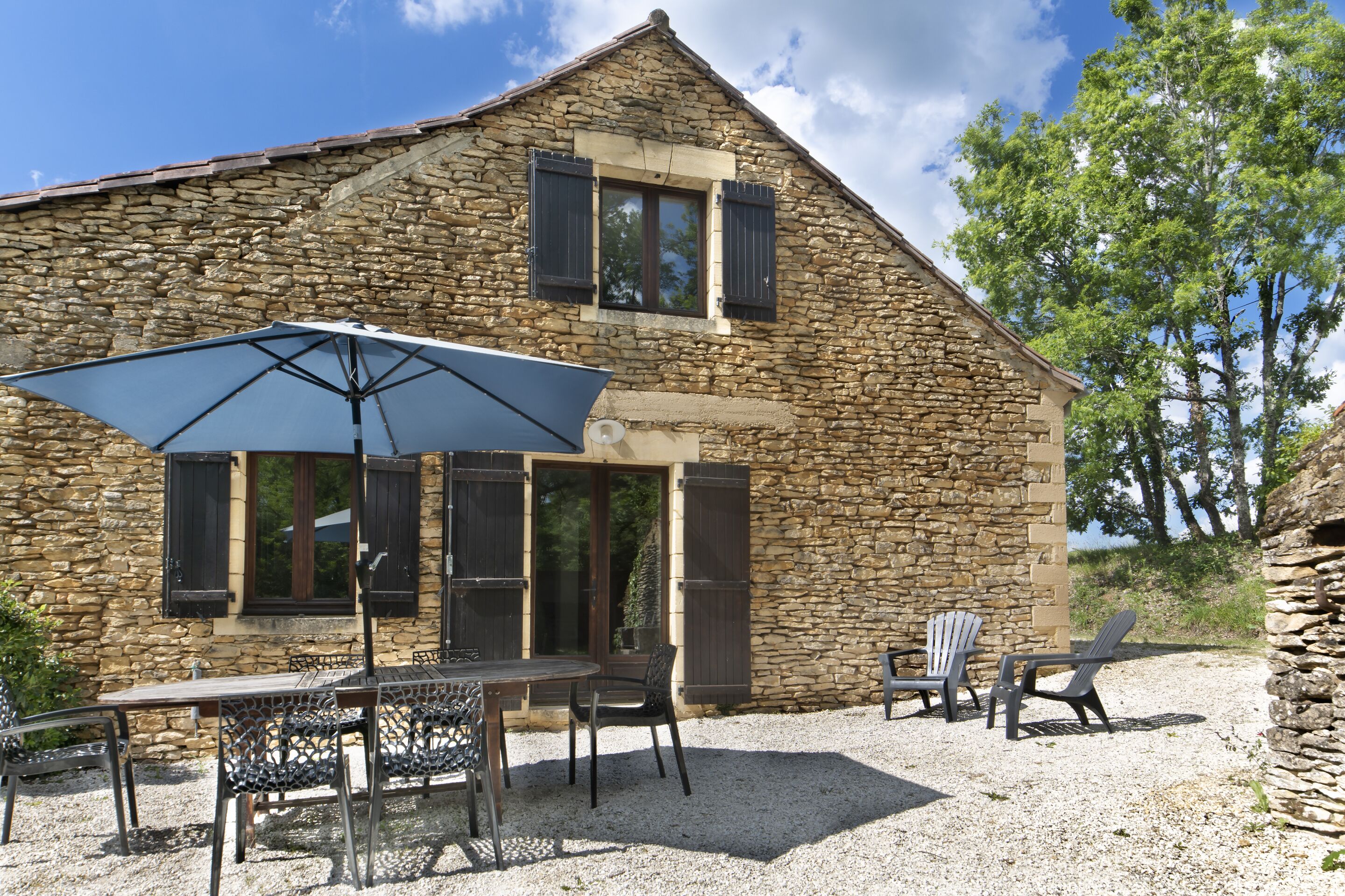 Un bâtiment en pierre doté d’une terrasse en gravier, de mobilier d’extérieur et d’un grand parasol.