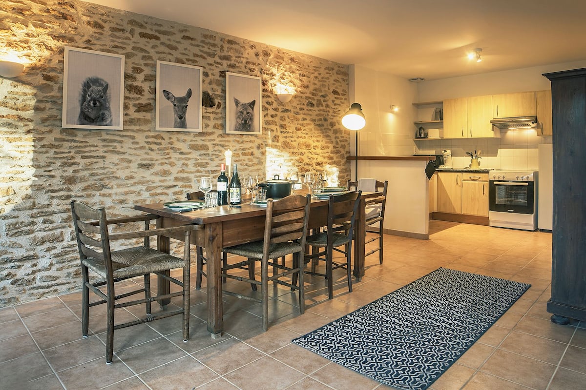 A dining area with a stone wall, wooden table, chairs, and framed animal pictures.