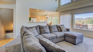 Amplia sala de estar con un sofá modular grande, una cocina al fondo y vistas al exterior.