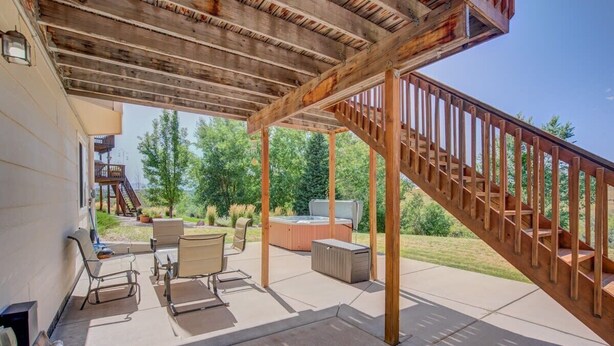 Un porche cubierto con mobiliario exterior, un jacuzzi y una escalera de madera.