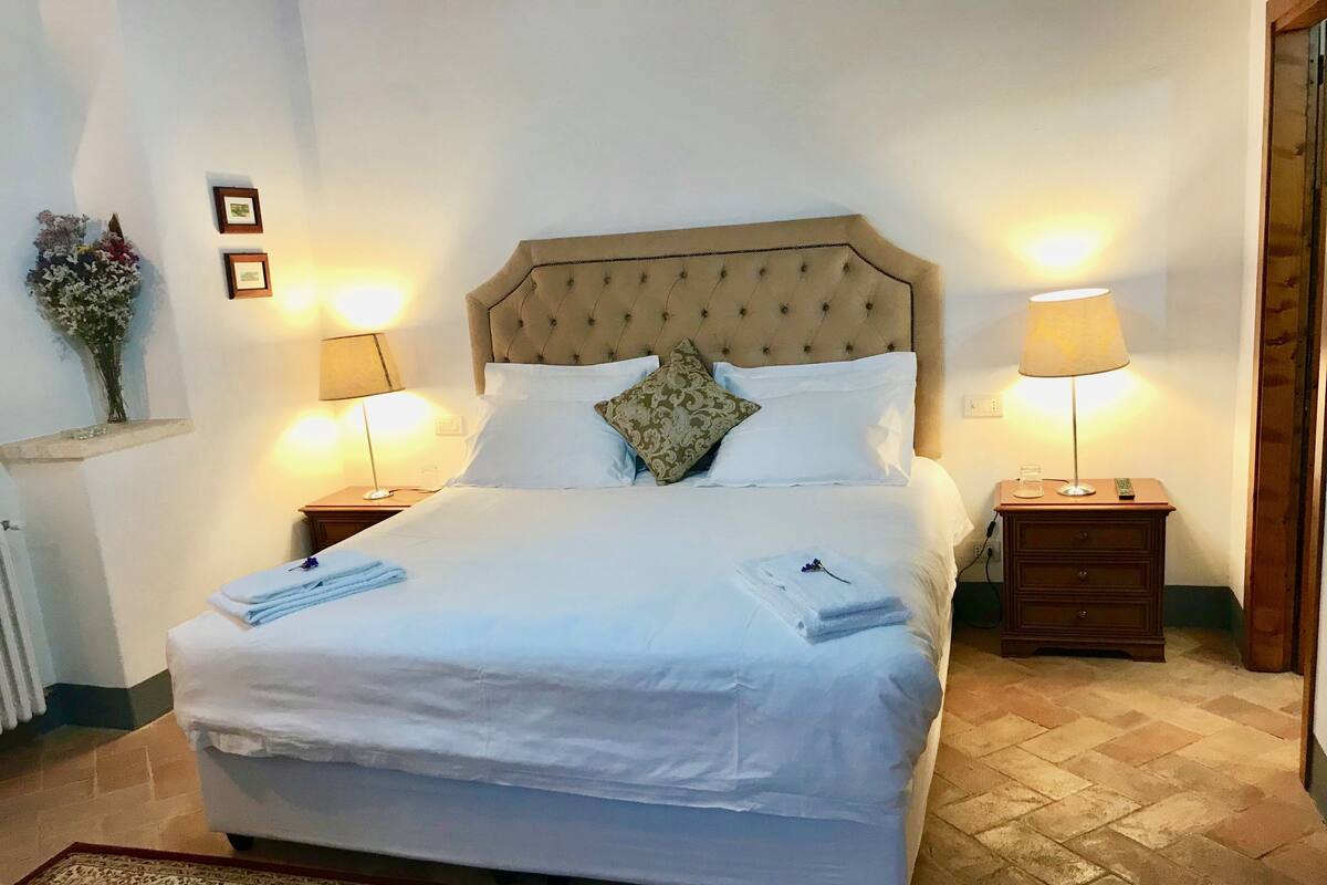 Ein ordentlich gemachtes Bett mit weißen Leinen, zwei Nachttischlampen und einem dekorativen Kissen.
