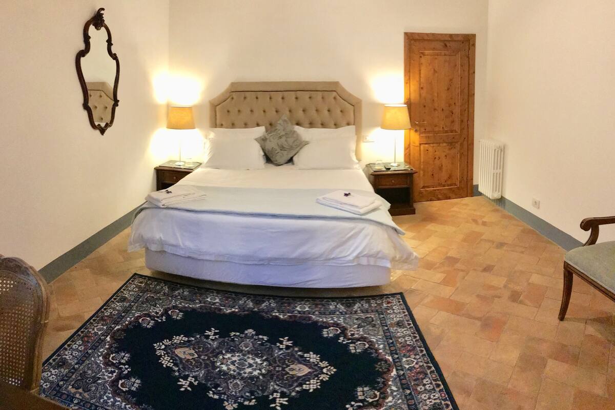 Ein ordentlich bezogenes Bett mit weißen Leinen, zwei Nachttischlampen, eine Holztür und ein gemustertes Teppich auf dem Boden.